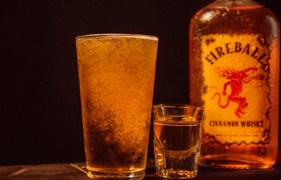 Tall glass of Pumpkin Ale, a shot of Fireball and a bottle of Fireball in the background.