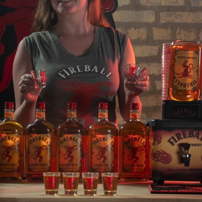 Download Bartender holding empty shot glasses with multiple Fireball Bottles and dispenser on counter