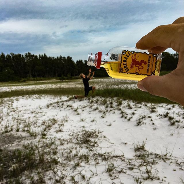 Man kneeling in snowy field while hand pours Fireball from  small bottle above