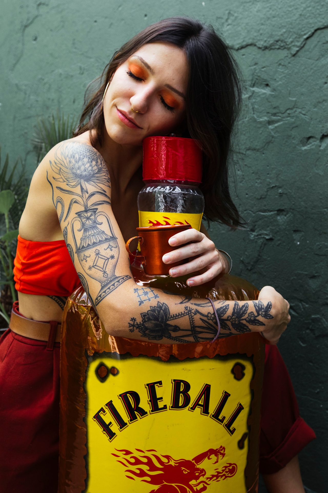 Woman hugging an inflatable bottle of Fireball whilst holding a mug